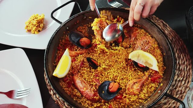 Pan of just cooked paella de marisco served on table in restaurant with pieces of lemon and spoons.