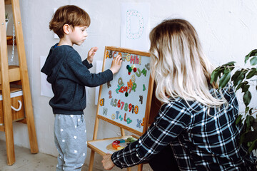 Little boy and educator playing and studying numbers, letters and alphabet on magnetic board in...