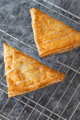 Apple turnover, freshly cooked, cooling down on a metal cooling rack. On a dark stone background
