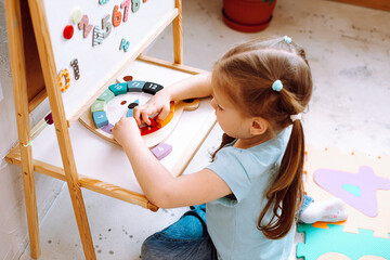 Little girl folding constructor and studying numbers on desk sitting on floor in playroom from above view closeup. Interesting game for kindergartners developing logic and intelligence
