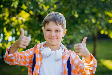 cute little caucasian boy with headphones and backpack showing thumbs up going to school