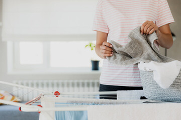Woman hanging clean wet clothes laundry on drying rack at home laundry room