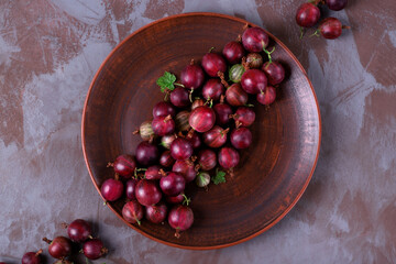 Red gooseberry on clay plate. Top view. Berry harvest
