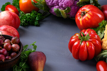 Harvest variation with assorted fruits and vegetables on gray table with copy space. Tomatoes, cauliflower, peach, fig and gooseberry in seasonal food composition