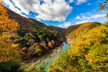 秋の京都・嵐山公園の亀山展望台から見た、紅葉に彩られた山の間を流れる桂川と背景の青空