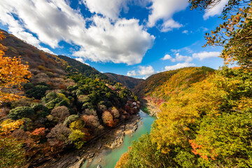 Fototapeta na wymiar 秋の京都・嵐山公園の亀山展望台から見た、紅葉に彩られた山の間を流れる桂川と背景の青空