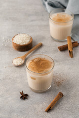 Homemade Horchata rice drink in a glass with ice and cinnamon stick on a gray concrete background. 