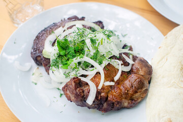 Appetizing grilled pork chop with onions and dill on the white plate. Juicy meat.