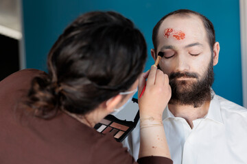 Artist using makeup effects to create zombie costume and scary dramatic corpse look. Man looking...