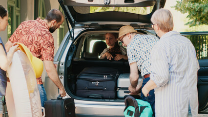 Casual family putting voyage trolleys in car trunk while getting ready for holiday vacation departure. People loading baggage and backpacks inside vehicle while going on summer citybreak together.
