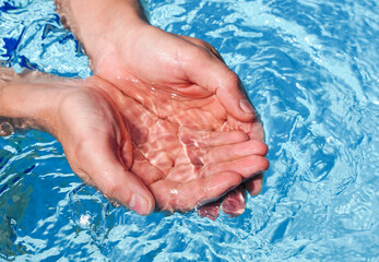 The hands cupped together submerged in clean clear blue water in swimming pool