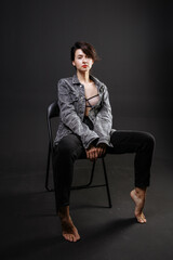 beautiful brunette girl in a jacket and jeans posing on a chair in the studio
