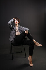 beautiful brunette girl in a jacket and jeans posing on a chair in the studio