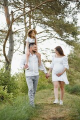 Happy pregnant couple with daughter in summer nature.