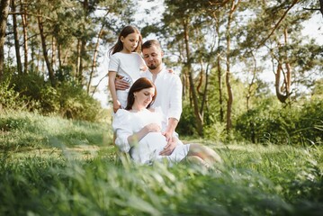 Fototapeta premium Happy family. Dad, pregnant mom and little daughter play games at sunset in summer in park.