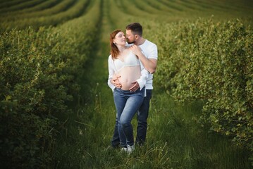 Happy and young pregnant couple hugging in nature