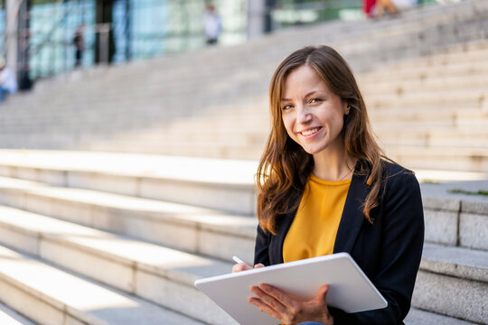 Smiling businesswoman with tablet PC sitting on steps
