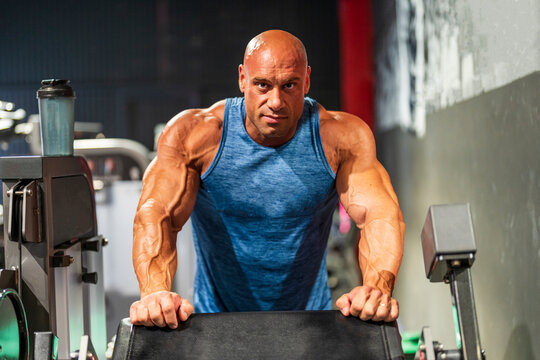 Bald bodybuilder leaning on exercise machine in gym