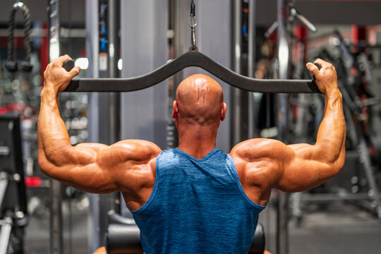 Muscular bodybuilder using lat pulldown machine in gym