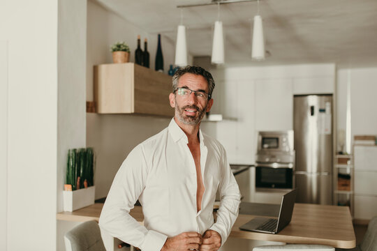 Businessman buttoning shirt in kitchen at home