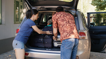Parents putting luggage in car trunk while unpatient daughter hurrying them. Positive family...