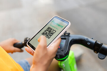 Young woman with electric push scooter making payment through smart phone