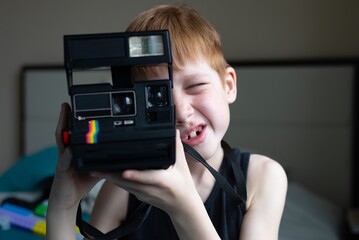 Child red-haired boy holds an old retro camera in his hands and makes a photo with a smile, children's hobby photography, life style portrait at home