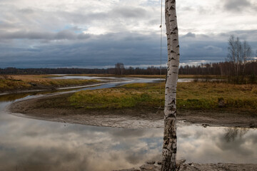 Obraz premium Autumn landscape with river bends on an autumn day. The birch grows on the banks of the river. The sky is reflected in the surface of the water