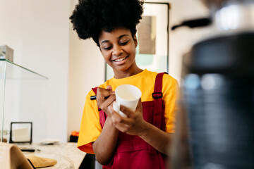 Smiling woman writing on disposable cup in cafe