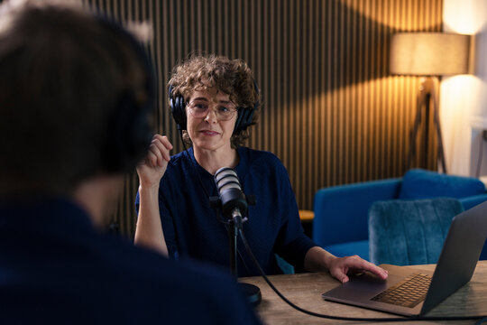 Radio DJ wearing eyeglasses and headset interviewing guest in recording studio