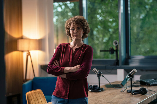 Confident radio DJ standing with arms crossed in recording studio