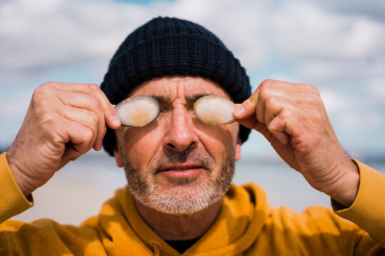 Mature man wearing knit hat covering eyes with seashells