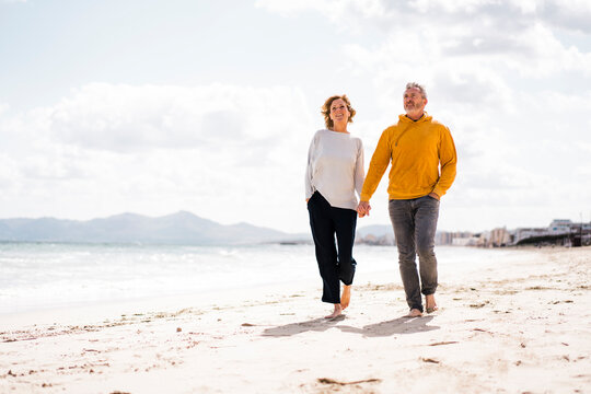Happy mature couple holding hands walking on shore at beach