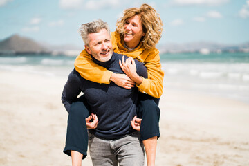 Happy man giving piggyback ride to woman at beach on sunny day