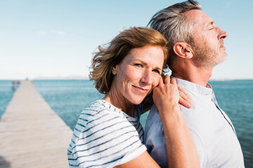 Smiling mature woman standing with man at jetty on sunny day