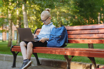 Fototapeta premium cute caucasian boy sitting on bench in park with laptop computer. Black screen