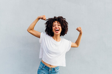 Cheerful young woman flexing muscles in front of white wall