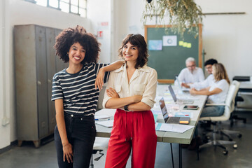 Smiling businesswoman with arms crossed by colleague in office