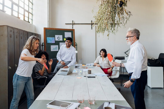 Businesswoman and manager playing table tennis in office with colleagues cheering in background