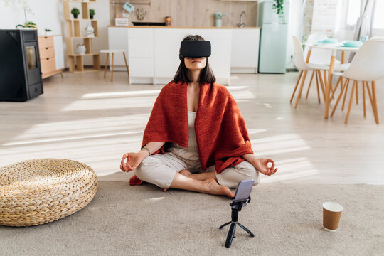 Woman wearing virtual reality headset practicing lotus position at home