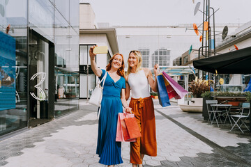 Happy friends with shopping bags taking selfie with smart phone in city
