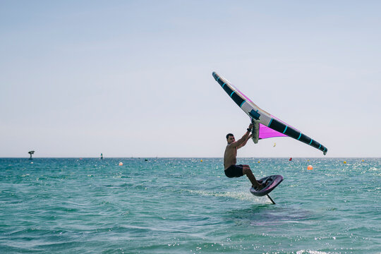 Young shirtless man practicing wind foil in sea