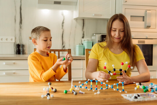 Mother and son holding molecules on table at home