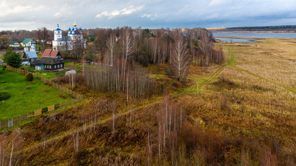 Aerial view of the village on a high hill above the river at sunrise in autumn. Aerial view. Residential buildings and a church, river bends, meadows, orange grass, trees at dawn. 