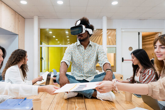 Businessman sitting on desk in conference room in office wearing VR goggles