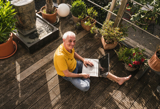 Smiling man with laptop sitting on terrace