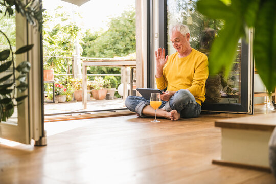 Smiling man doing video call through tablet PC sitting at home