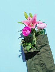 Army green jacket's sleeve arranged with exotic tropical flowers, creative layout on pastel blue background. Eco friendly fashion idea.