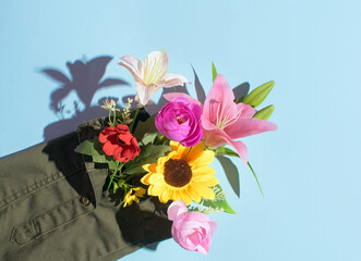 Army green shirt sleeve decorated with colorful flowers on pastel blue background. Creative peace inspired layout. 