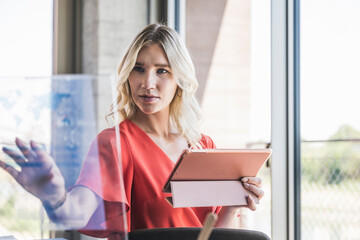 Businesswoman holding tablet PC touching transparent screen in office
